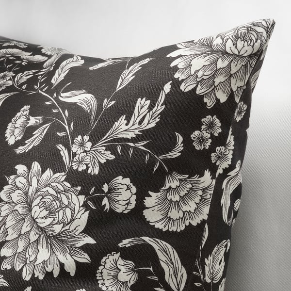Black pillow with white floral design, intricate details, smooth fabric, seen from side.