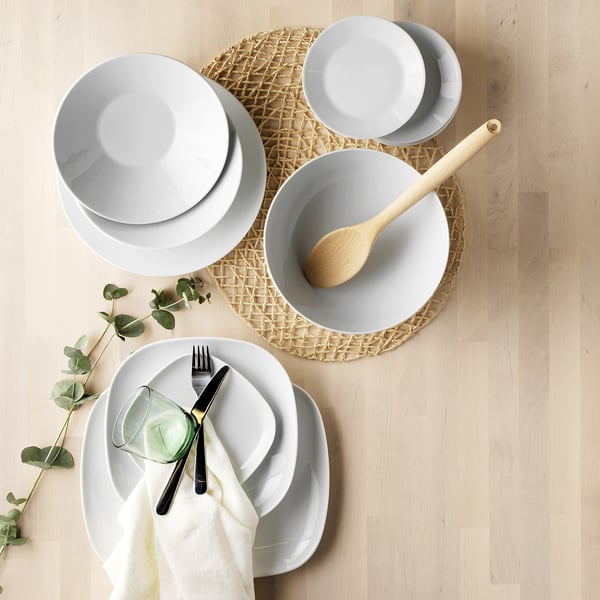 White dinnerware set on placemat; plates, bowl, spoon, glass, cutlery.