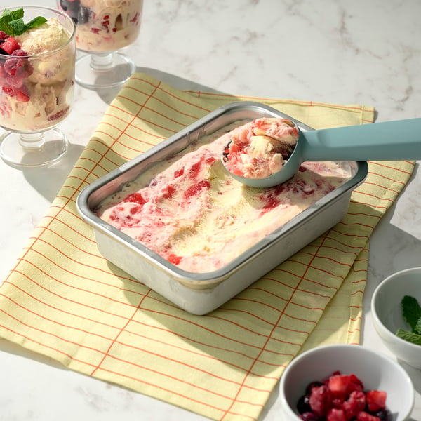 Ice cream tub with scoop on cloth next to berry bowls.