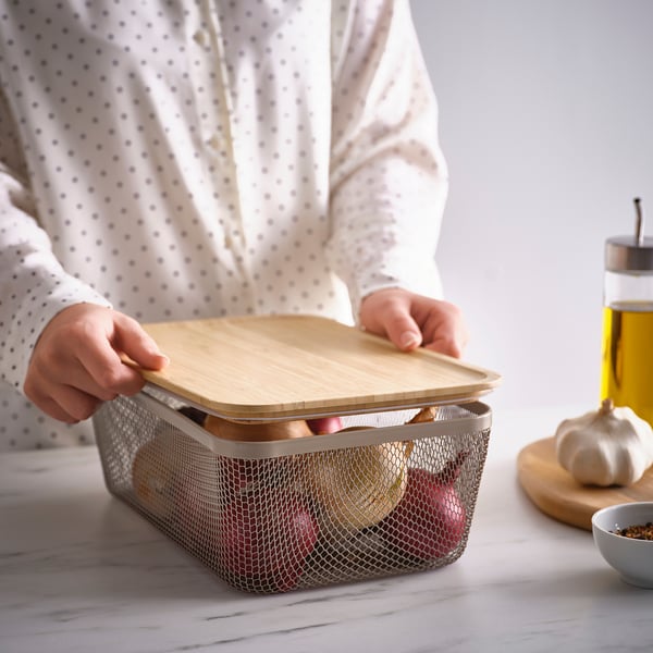 Person placing a bamboo lid on a mesh food container on a counter. The lid protects food, keeps it fresh, and can also serve as a coaster.