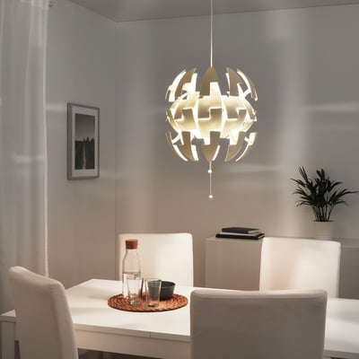 Modern dining area with IKEA PS 2014 light, table set with glasses and plants.
