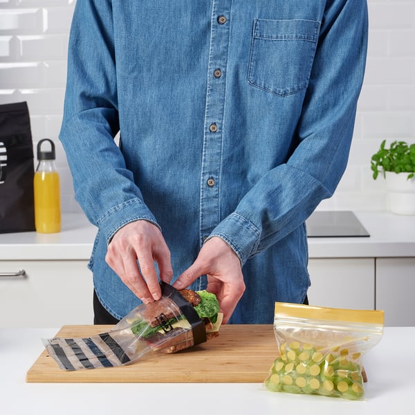 Packing sandwich in reusable plastic bag on wooden board. Alternatively: reusable bag being used to pack sandwich on cutting board.