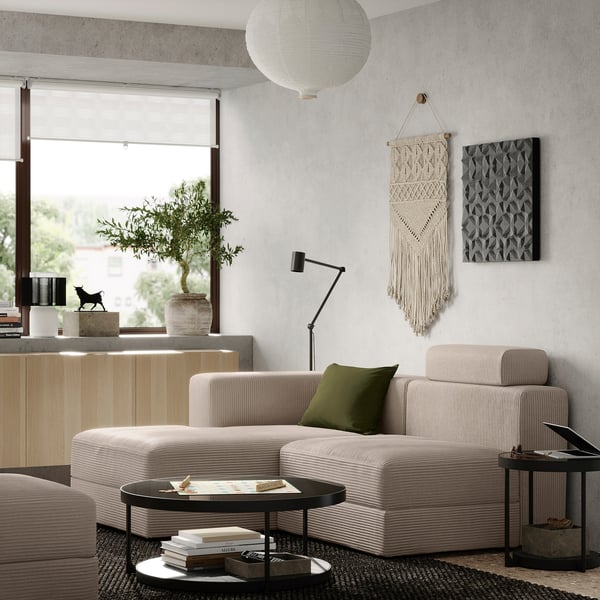 Modern living room with JÄTTEBO beige sofa, green pillow, wooden cabinets, and decorative wall hangings.