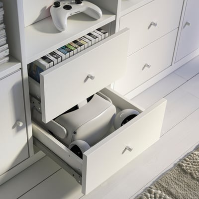 White KALLAX storage unit with open drawers holding gaming controllers, stack of games on top.