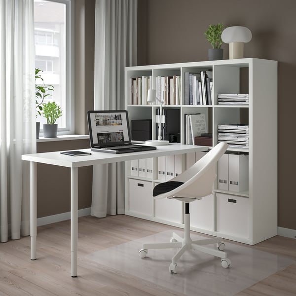 Modern minimalist home office with white KALLAX shelf unit, desk, and chair. Large window with sheer curtains, wooden floor.