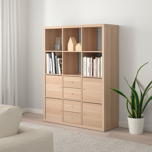 KALLAX shelf unit with books, decor, and plant. Beige sofa partially visible.