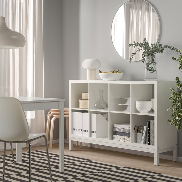 White KALLAX shelves with books, bowls, vases, and a lamp in a minimalist room.