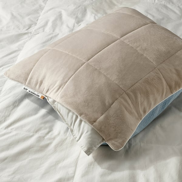Pillow protector with cooling blue side and warming beige side on bed.
