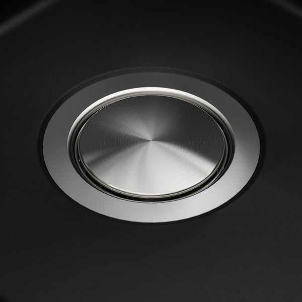 Round stainless steel lid fitted in black sink, reflecting light, showcasing smooth, polished surface.