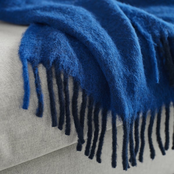 Blue throw blanket with fluffy texture and fringe detail.
