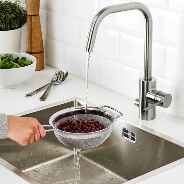 Hand rinsing beans in sink with KLOCKREN colander, streamlined tap, set on modern kitchen counter.