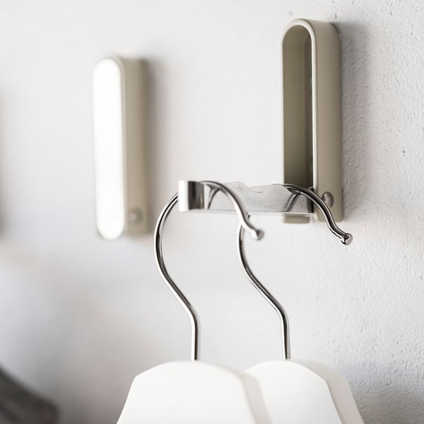 A silver KLYKET hook mounted on a white wall, holding a white hanger.