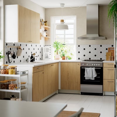 KNOXHULT kitchen: light wood cabinets, marble top, stainless stove & hood. Black hex tiles, green plants. Modern, spacious l-shape.