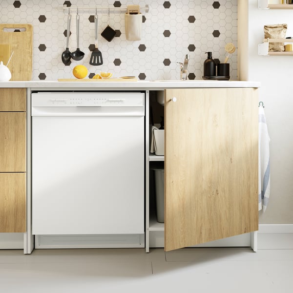 Modern kitchen with light wood cabinets, a white dishwasher, and hanging utensils.