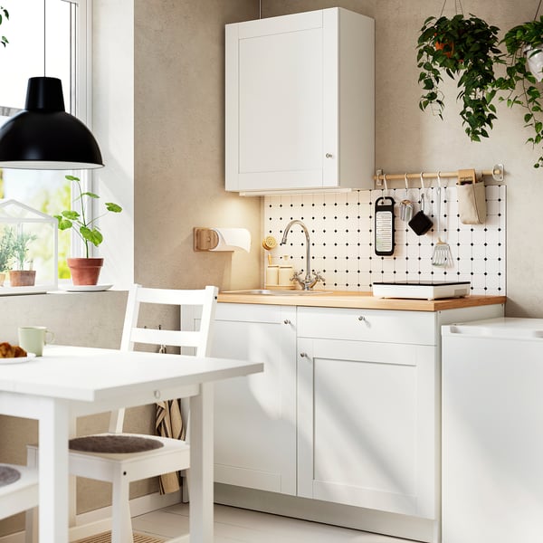 Compact white kitchen with oak counter, sink, hanging utensils, and a cosy breakfast setup. Efficient for small spaces.