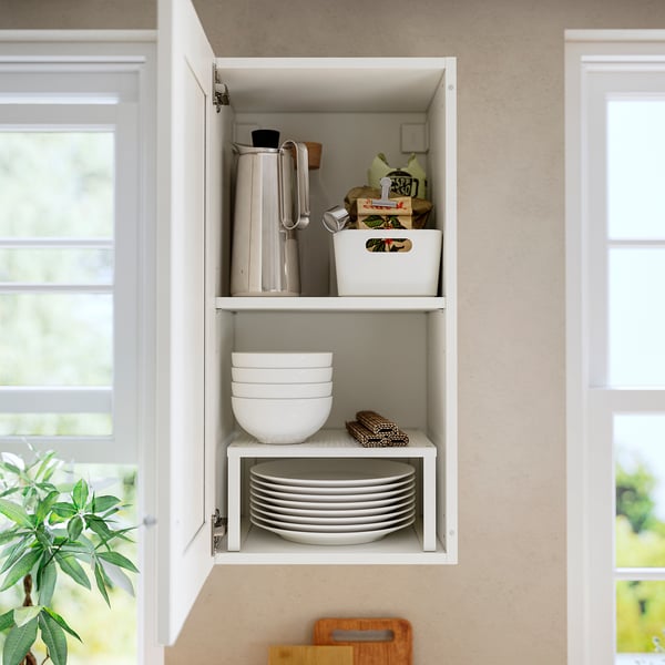 Open kitchen cabinet storing plates, bowls, and utensils, with a white framed door.