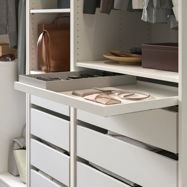 White KOMPLEMENT closet organiser with slid out tray holding wallets and accessories, surrounded by clothing and a hanging bag.