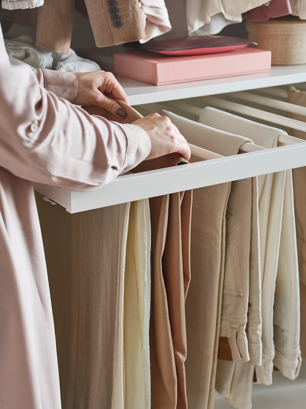 A person organising light-colored trousers on a white KOMPLEMENT trouser hanger.