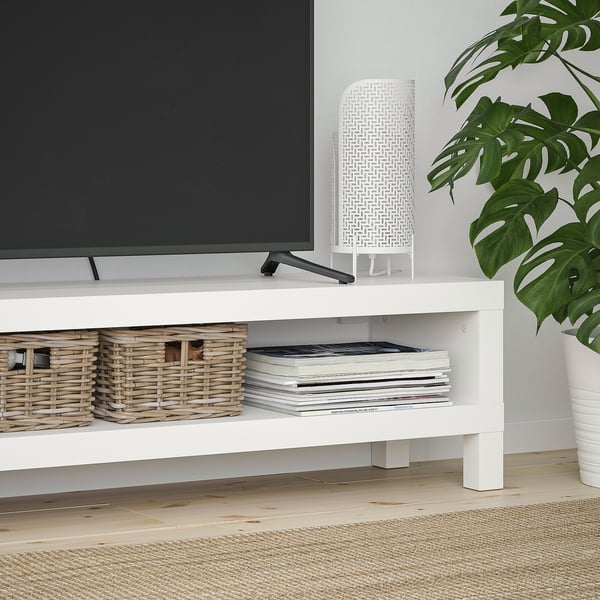 Minimalist white tv stand with open shelves, holding baskets and magazines, supporting a flat-screen tv and modern decor.