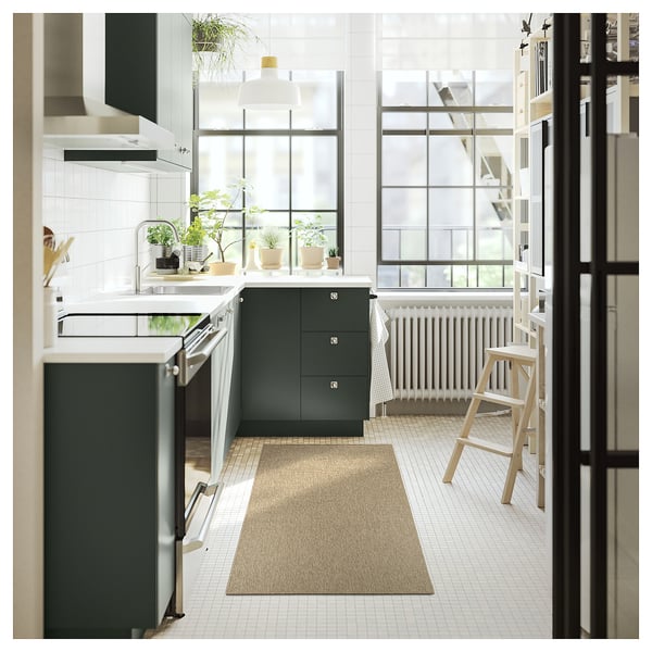 Modern kitchen with LÄTTBETONG beige runner rug, dark green cabinets, white tiles, and wooden stools by large window.