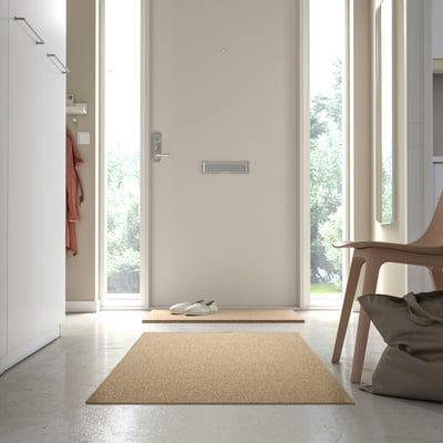 Beige LÄTTBETONG rug in hallway, near door and chair, complements minimalist decor.