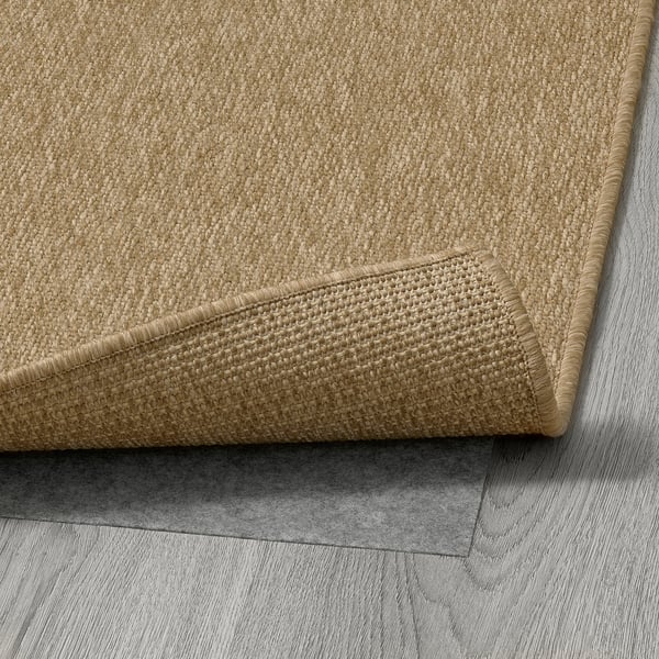 Close-up of beige woven rug, showcasing its textured surface and sturdy, folded edge, laid on grey tiled floor.