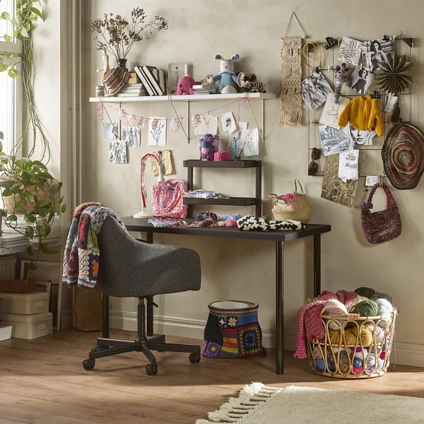 Craft workspace with LAGKAPTEN dark desk, chair, yarn basket & shelves holding supplies, art & plants.
