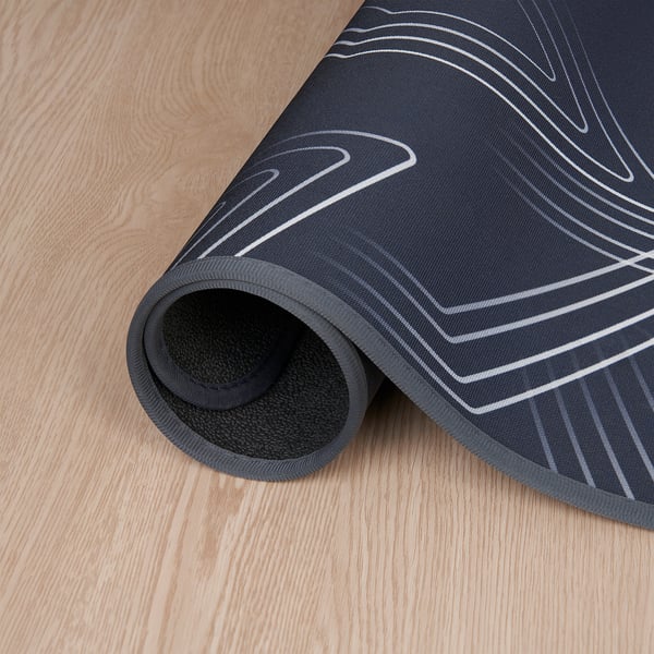 Black gaming chair mat with white lines, rolled out on wooden floor, protects floor and dampens sound.