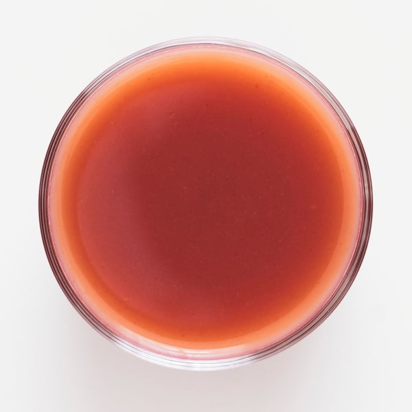 A clear glass bowl filled with a thick, red berry fruit smoothie with a glossy texture. Fresh strawberries, raspberries, and blueberries highlighted.