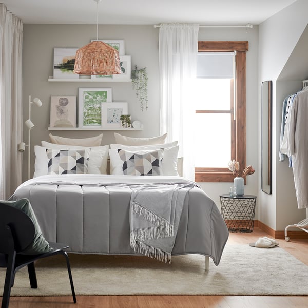 Grey bed, geometric pillows, large window, lamp, rug, wardrobe.