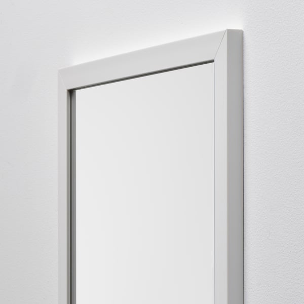 A sleek, modern mirror with a plain white frame, securely mounted on a pristine white wall, reflecting light for added depth.