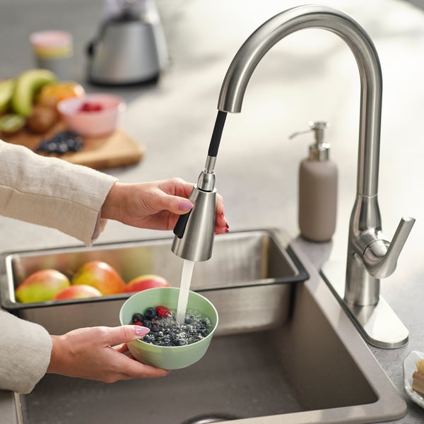 Person washing berries in kitchen sink with MACKSJÖN tap, using pull-down spray function.