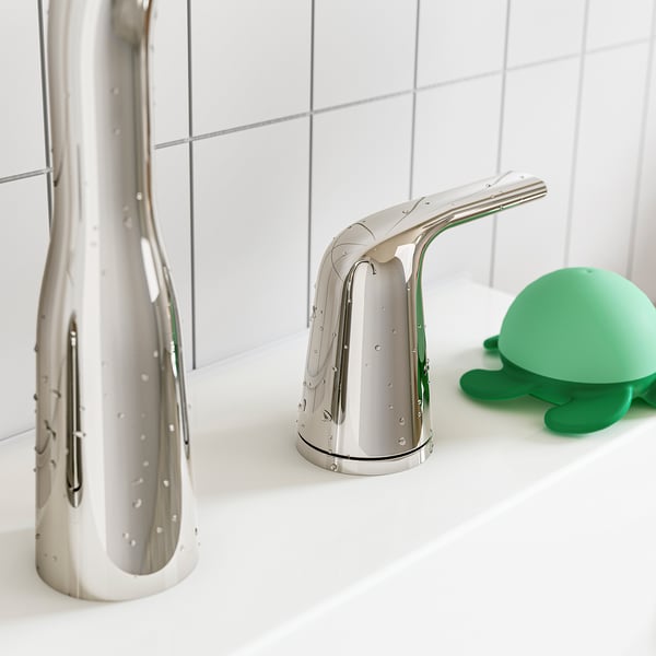 Modern chrome tap on white sink with green turtle soap dispenser.