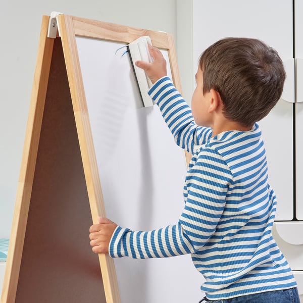 A young boy draws on a wooden easel with a whiteboard using a MÅLA pen.