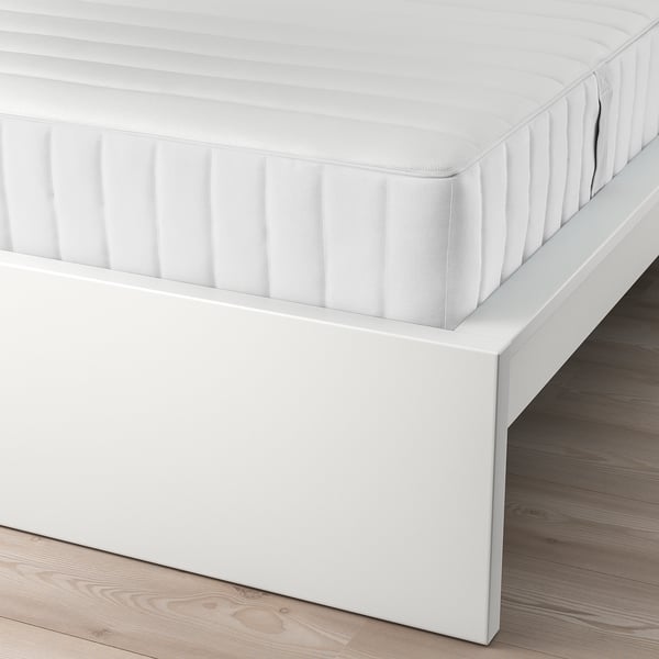 White bed frame with adjustable sides holding a quilted mattress, on wooden floor. Part of IKEAs MALM series.