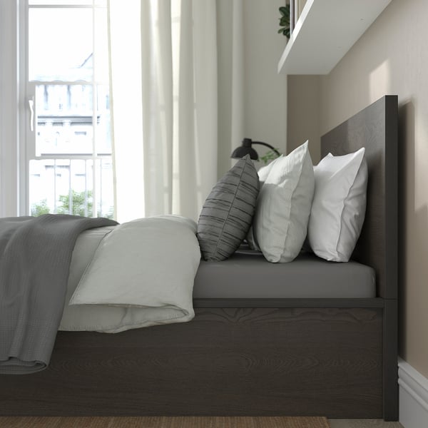 Bedroom with MALM bed, featuring a dark headboard, grey linens, and multiple pillows. Large window offers natural light.