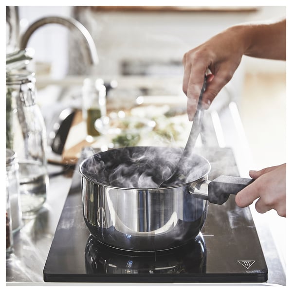 Cooking with MIDDAGSMAT saucepan on induction stove. Stainless steel, sleek design, emitting steam.