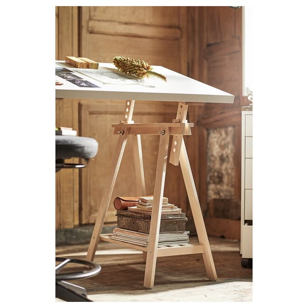 A white wooden artists trestle with adjustable tilt, sitting in a cosy, rustic room.