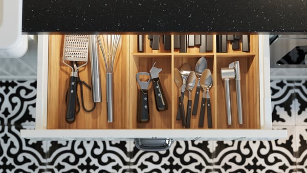 Kitchen drawer with utensils and knives, lit, black handles, wooden front.