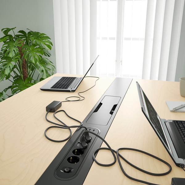 Modern office table with built-in power sockets, neatly organised with laptops, a plant, and a mug.