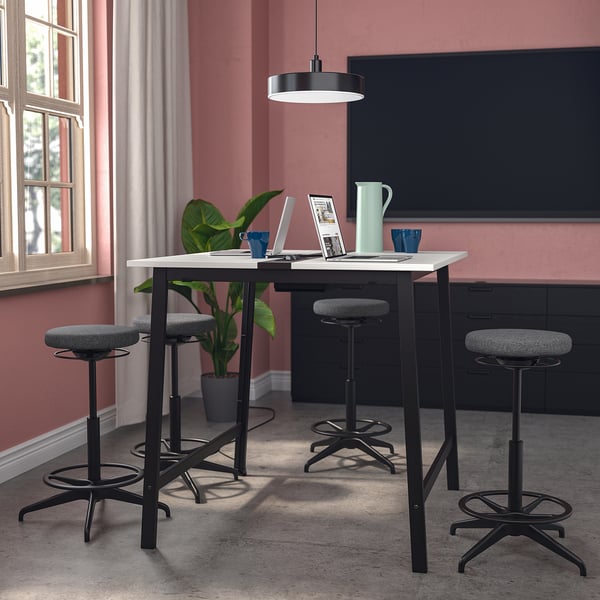 MITTZON conference table with stools, black with white top, against pink wall, workspace with tech, window.