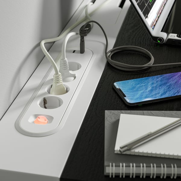 Desk with built-in power sockets and cable management. A smartphone rests on the desk, highlighting the charging stations functionality.