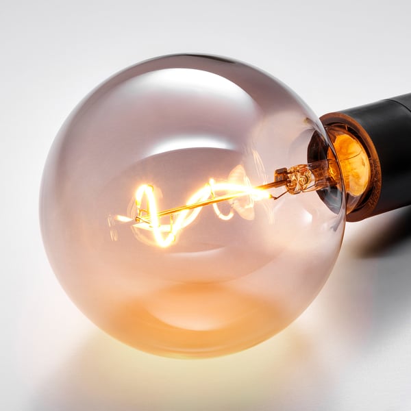 Close-up of a warm, round light bulb with a spiral filament glowing inside smoked glass.