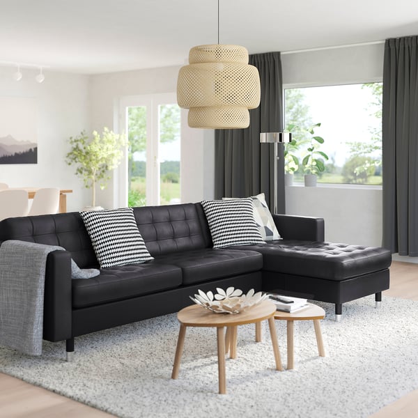 Modern living room with black leather l-shaped sofa, wooden side tables, white rug, and large window. A stylish and cosy setup.