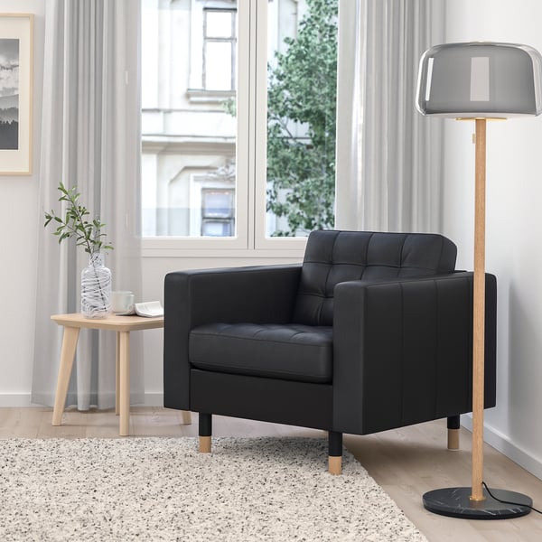 Modern living room with black armchair, floor lamp, side table, plant, large window.