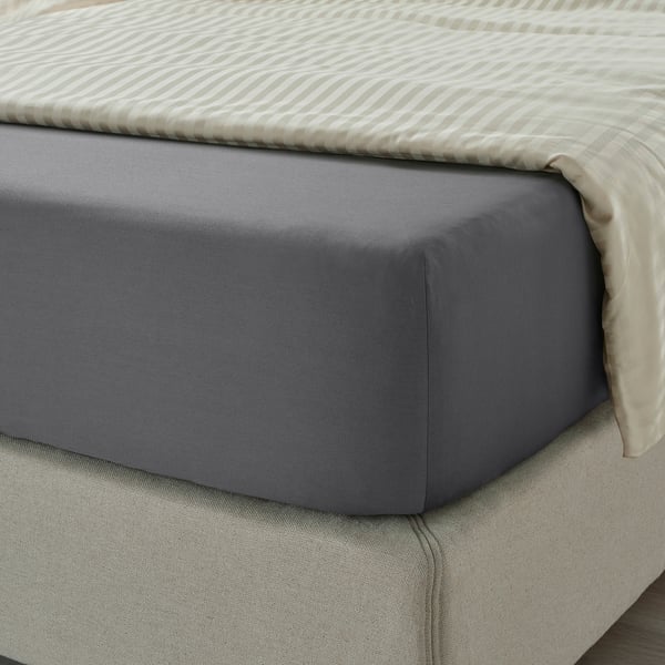 Bed with dark grey sheets, smooth & lustrous, tucked on a textured bed frame.