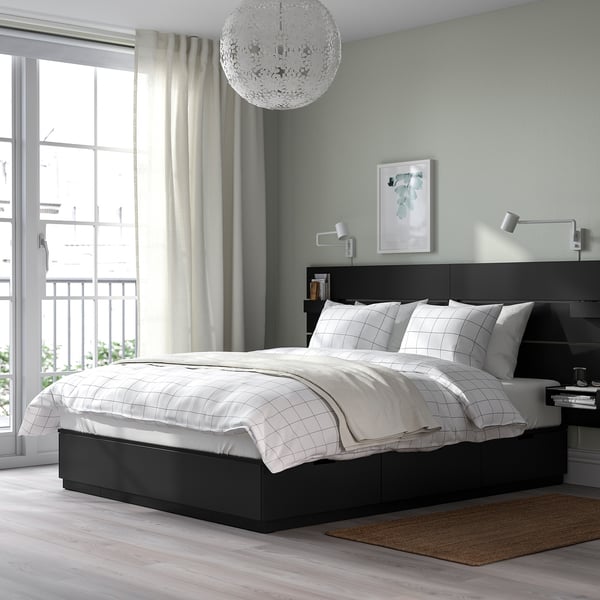 Modern bedroom with black NORDLI bed, white bedding, large window, chandelier, lamps, art, and rug.