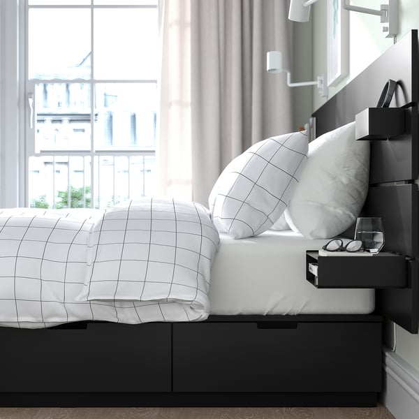 A modern bed with a black frame and white grid-patterned bedding. It multiple drawers for storage and a headboard with built-in shelves and lighting.