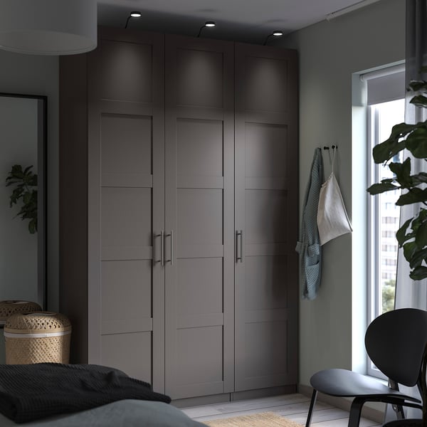 Modern bedroom PAX grey wardrobe with sleek handles and integrated lighting, alongside a black chair and wicker basket on a wooden floor.