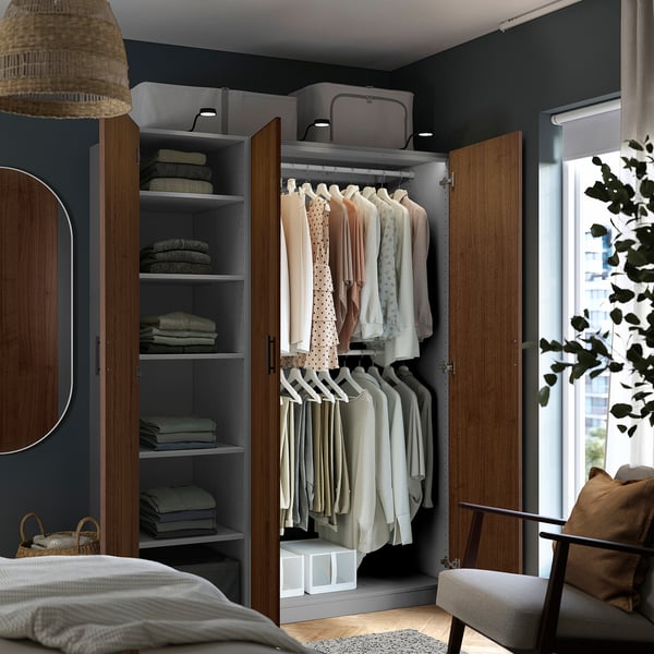 Modern, open closet hanging clothes and neatly folded sweaters on shelves. Wooden frame with grey interior, lit by ceiling lights.